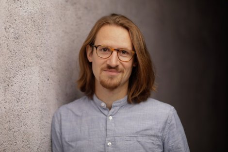 Portrait eine Mannes mit Brille und halblangen Haaren, hellblaues Hemd