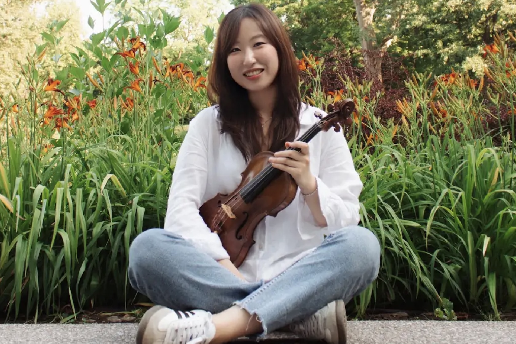 Eunsong Jung with violin in front of a flower bed